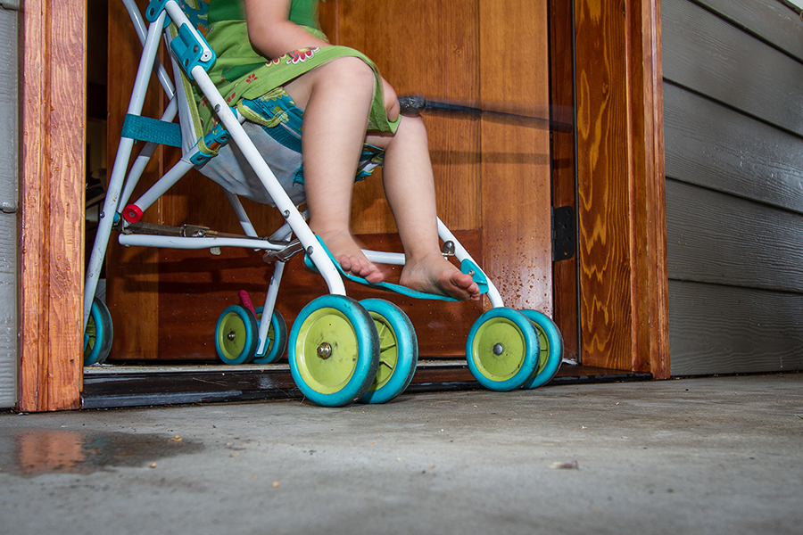 A young child's feet and the bottom of a stroller are visible as it is wheeled out of the front door.